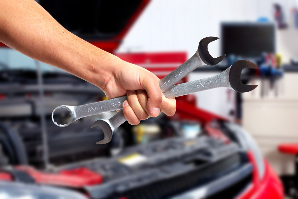 a hand holding wrenches in front of a red car